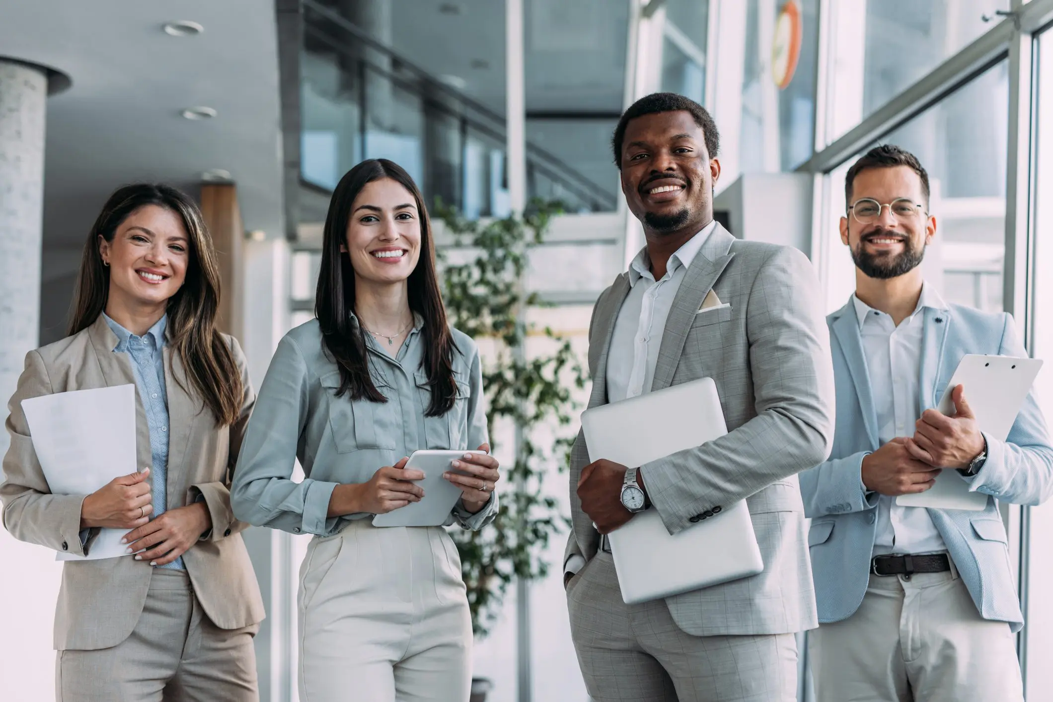 A group of four diverse professionals smiling in an office hallway.
