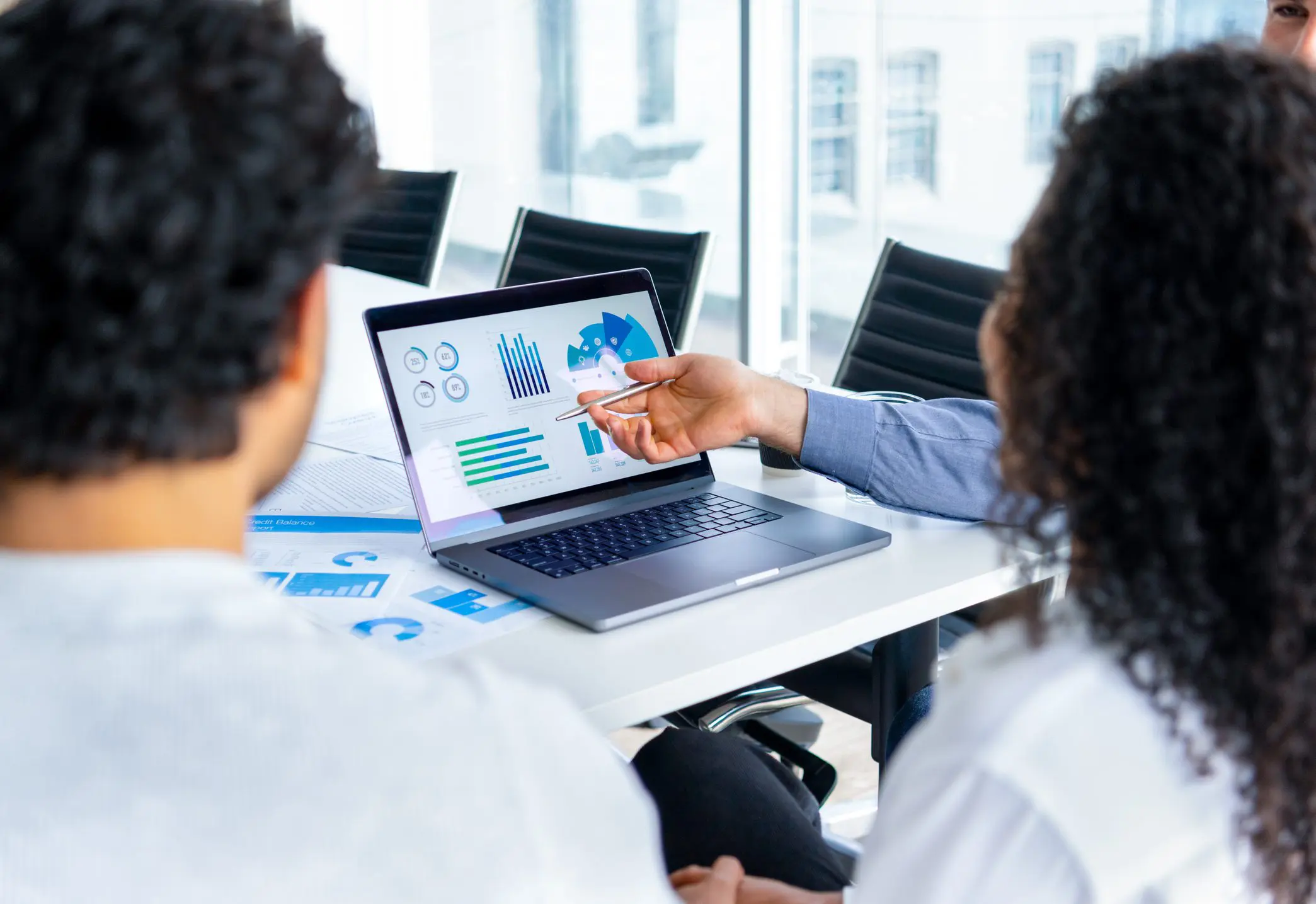 Two professionals analyzing charts and graphs on a laptop screen during a meeting.